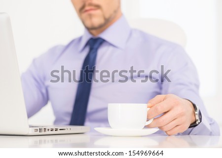 Businessman at work. Cropped image of confident young man in formalwear working at the computer and drinking coffee