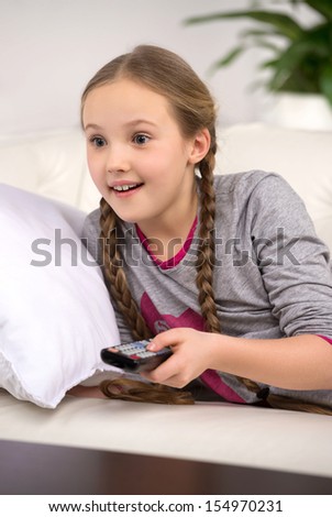 Cute girl at home. Cheerful little girl watching TV and smiling