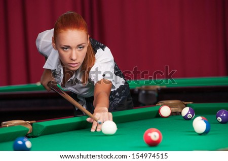 Woman playing pool. Confident young woman aiming the billiard ball with cue