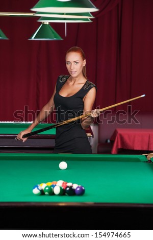 Sexy pool player. Beautiful young female pool player in black dress holding cue and looking at camera