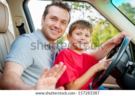 Father and son is sitting at the stearing wheel and smiling at the camera