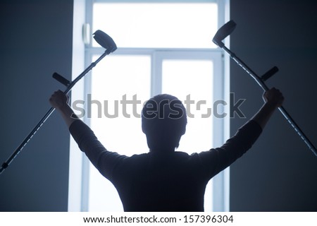 Black silhouette on the white window. man is raising crutches