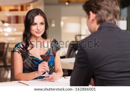Seducing beautiful woman looking at her lover with wine glass. Having romantic talk