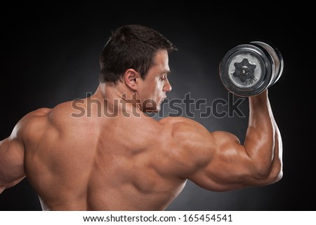 Back view muscular man lifting dumbbell up. Training isolated over black background