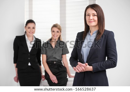 Smiling confident middle aged business woman leading young female business team. Standing together in bright modern office