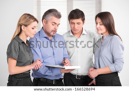 Handsome adult business man showing something on documents. Standing together in bright modern office