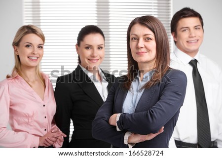Successful adult business woman standing with crossed arms. Happy successful business team standing on background