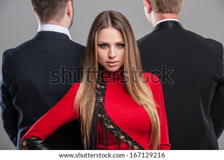 Fashion shoot Sexy blond stylish girl looking at camera. Two men in black suite standing on the background