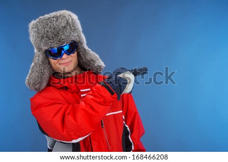 Confident successful man in winter hat and sport coat. Pointing with finger at blue background