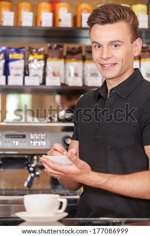 handsome barista writing check and smiling. attractive male making coffee and watching