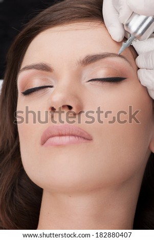 beautiful young lady getting tattoo. professional tattooist making eyebrow make up