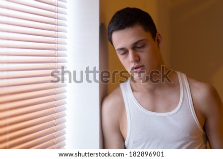 drug addict standing by window and sleeping. young man leaning against wall