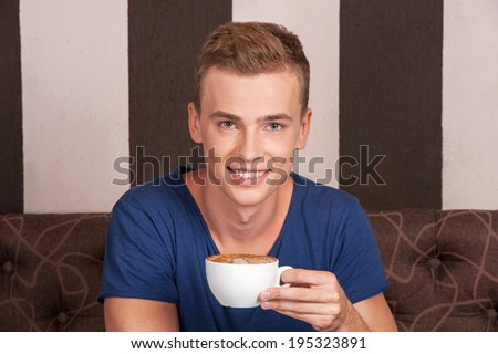 handsome young man sitting on couch. attractive guy drinking coffee and smiling