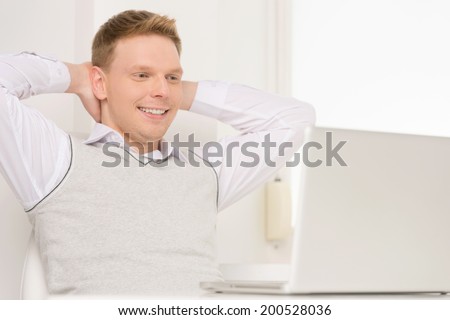 young man sitting in chair and smiling. handsome guy watching movie on laptop