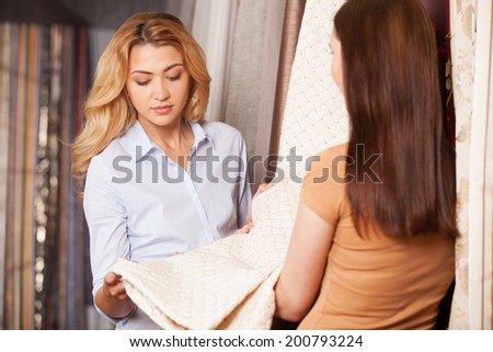 blond girl looking at material and thinking. brunette woman back view standing