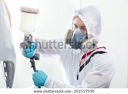 young man painting using airbrush. man wearing respirator and white hood