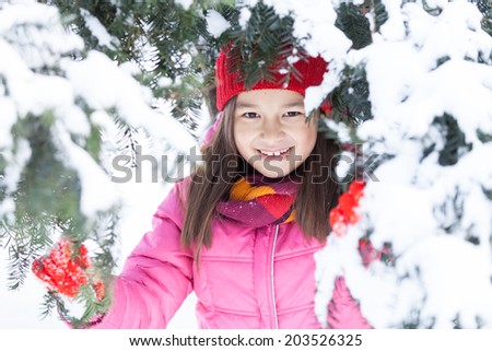 little girl hiding in pine tree. sister standing on snow under branches and smiling