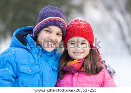 sister and brother smiling and hugging outside. boy and girl standing in park and looking into camera