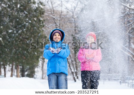 boy and girl throwing snow into air. two children playing in park and smiling