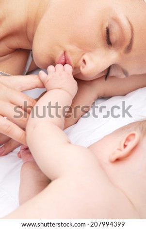 young mom kissing baby hands. little baby sleeping on bed with mom