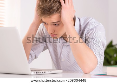 Young man sitting at table and using laptop. tired guy looking at screen and reading