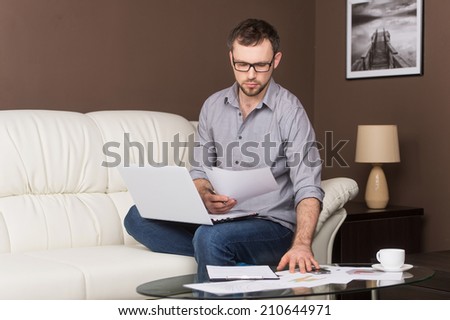 young man looking at paper in glasses. portrait of man sitting on sofa and holding documents