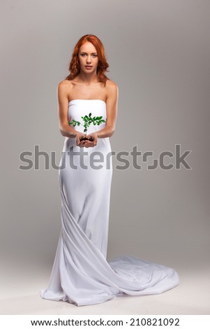 Closeup on beautiful calm woman holding plant in her hands. Sexy young girl covered with white sheet