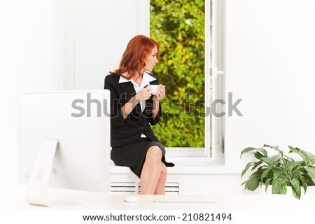 Pretty office girl sitting on windowsill. red hair girl enjoying cup of coffee and view