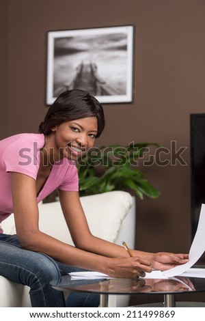 young african girl learning at home and smiling. pretty black woman sitting on sofa and writing on table