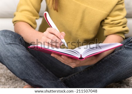 Woman student sitting on carpet and writing. closeup view of girl hand making notes in textbook
