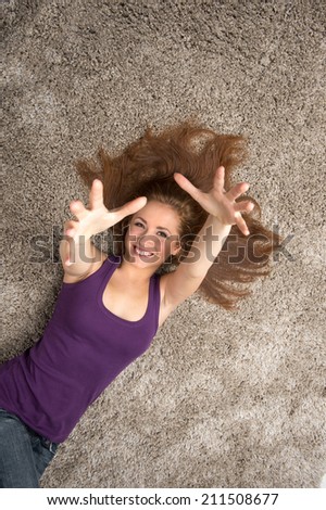 Relaxed woman lying on floor indoors and holding hands up. Beautiful young woman lying on floor