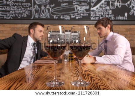 two friends sitting in cafe and eating lunch. two glasses of wine standing on foreground in restaurant