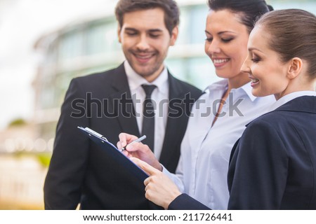 Young smiling business women and business man. three people looking at folder outside