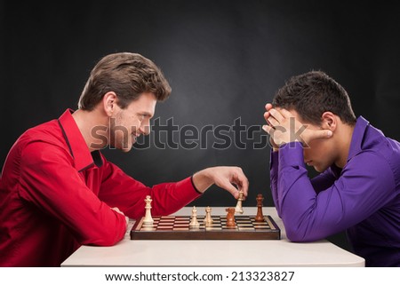 friends playing chess on black background. smiling young man moving chess piece