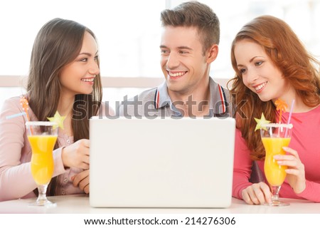 front view of three students using laptop. friends drinking juice at coffee shop