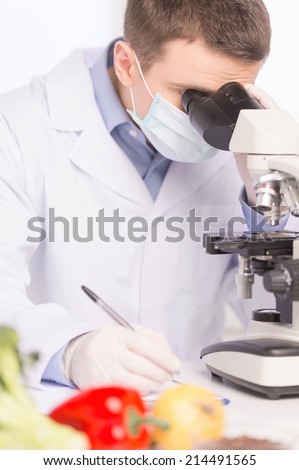 young man studying chemical elements in laboratory. blurred portrait of fruits lying near microscope
