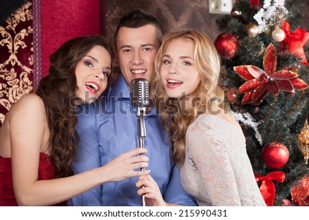 Photo of funny guy singing at party. two beautiful happy girls standing near by