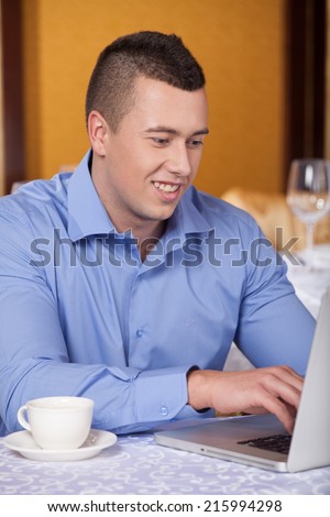 closeup of handsome man sitting in cafe and drinking coffee. guy using laptop computer and smiling