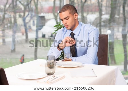 young man waiting for woman in restaurant. woman late to date and guy looking at watches