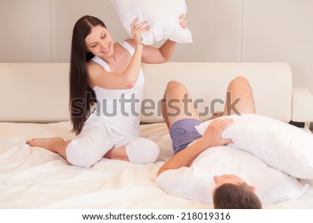 Couple fighting together with pillows in bed. Portrait of happy loving couple having pillow fight in bed