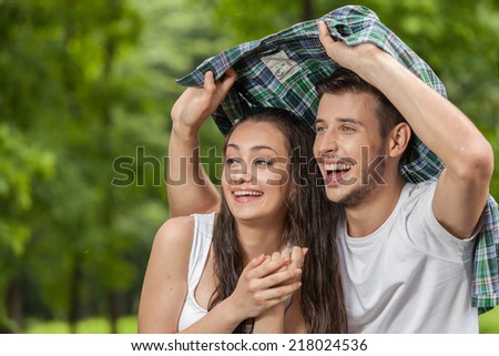 Happy young woman covering from rain. Woman and man walking under shirt in rain