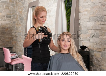 Stylist drying hair of smiling female client at beauty salon. Young female beautician giving new hair style to woman at parlor