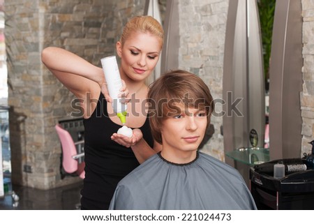 blond hairstylist female with hair mousse spray. young attractive man sitting in hair salon