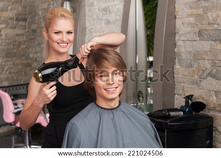 Blond female hairdresser drying hair of man client. profile of happy man sitting in hair salon and smiling