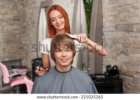 Female hairdresser cutting hair of man client and smiling. happy man sitting in hair salon and looking into camera