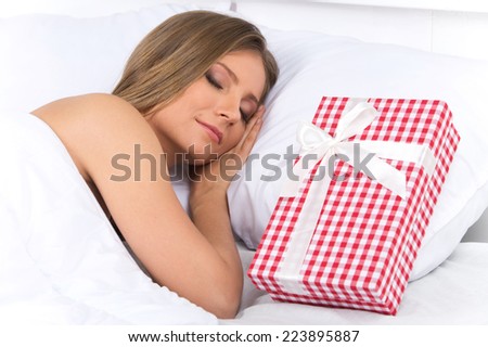 Asleep woman has surprise present waiting for her in bed. closeup on beautiful young woman sleeping on bed with presents