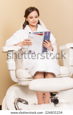 Young woman receiving pedicure in hairdressing salon. Woman sits in hairdress salon and reading magazine