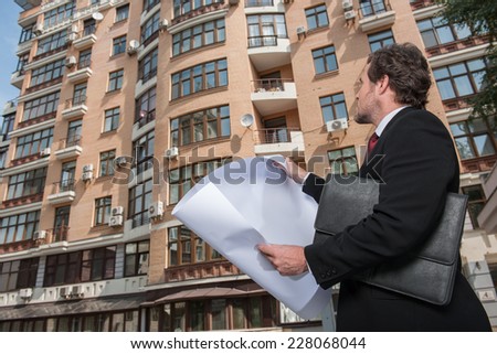Architect looking at plan and apartment building. Architect reviews plans and holding plan