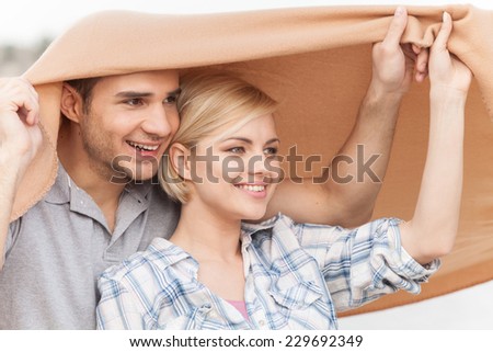 Attractive young couple sitting on beach at summer. happy woman and man sitting under blanket and smiling