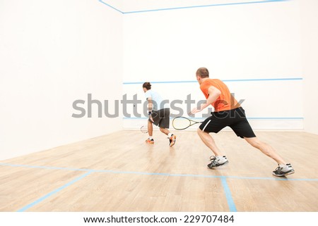 Two men playing match of squash. Back view of squash player in action reaching on squash court
